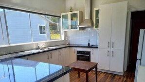 Une cuisine moderne dotée d’un grand îlot central, de meubles blancs, d’un four encastré et d’une fenêtre offrant une vue sur l’extérieur.