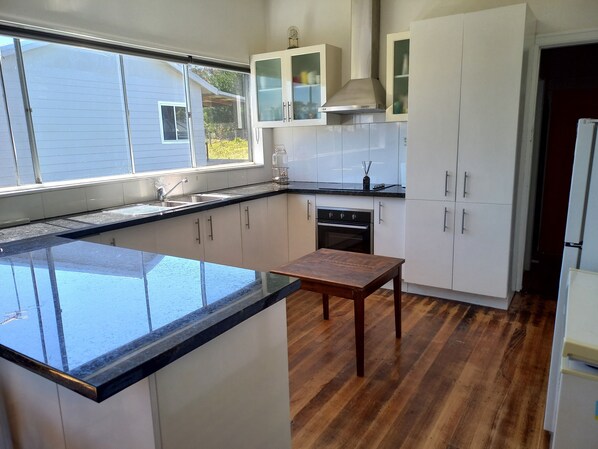 A modern kitchen with a large island, white cabinets, a built-in oven, and a window providing a view of the outside.