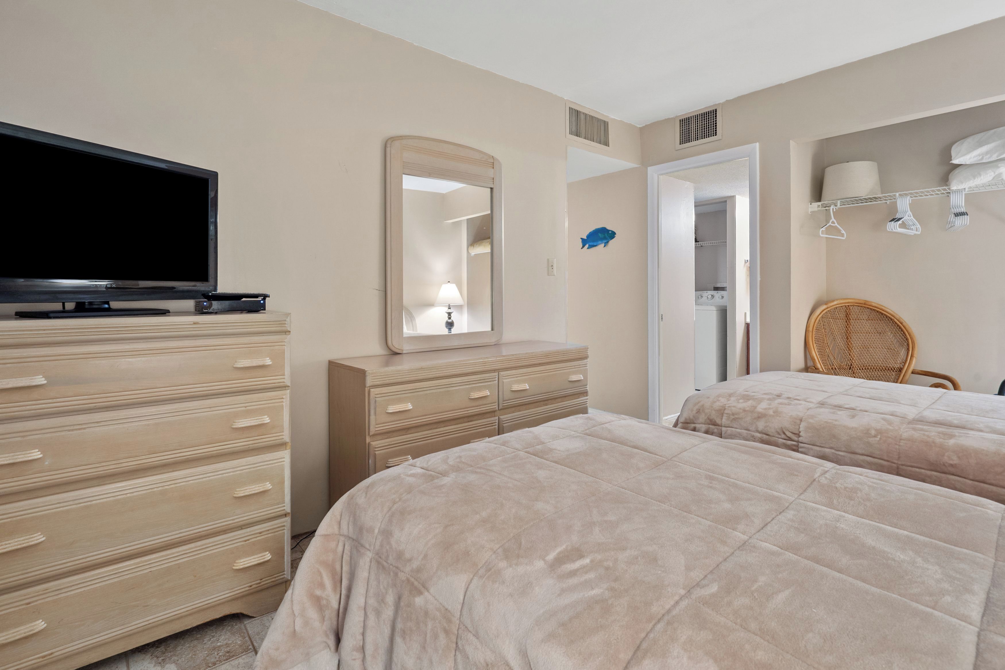 Une chambre avec deux lits, une commode, un téléviseur, un miroir, une armoire et une chaise.