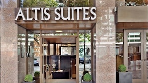La entrada a Altis Suites, con una puerta de vidrio y un alero de madera.