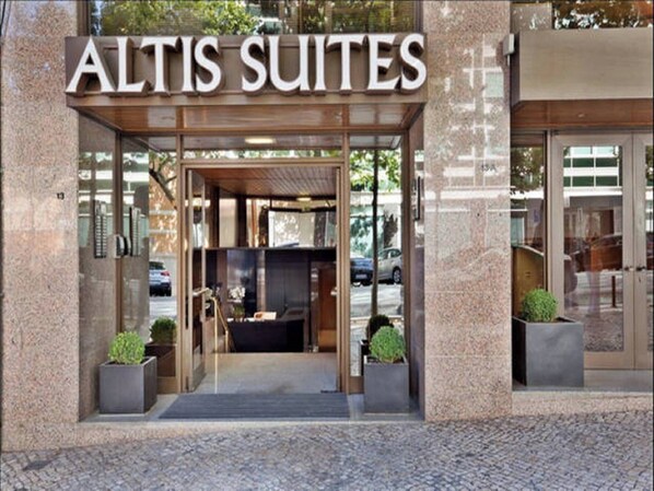 The entrance to Altis Suites with a glass door and a wooden overhang.
