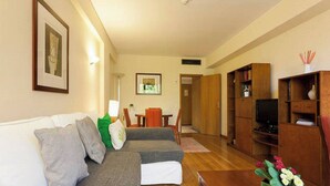 Una sala de estar con sofá, una mesa de centro y un mueble para la televisión. Hay un comedor con una mesa y sillas.