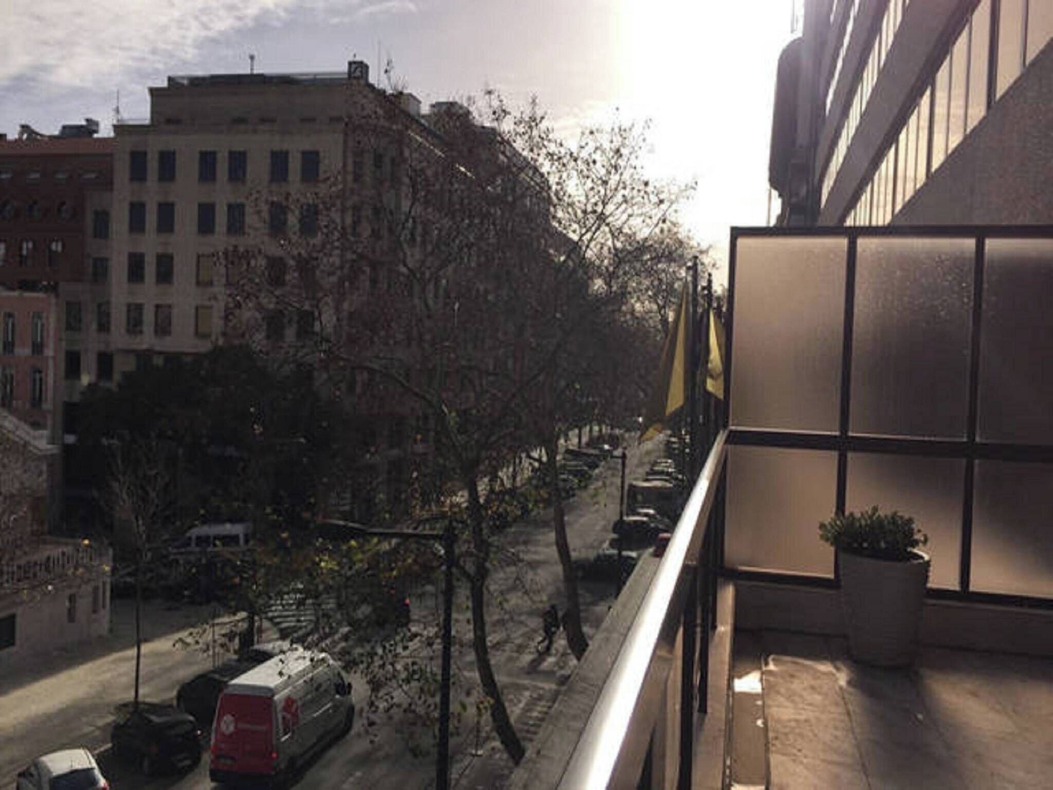 A view from a balcony overlooking a street with parked cars and trees.