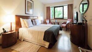 Habitación de hotel con una cama grande, un escritorio, una silla, un aparador y un televisor.