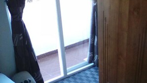 A hotel room with a bed, a wooden wardrobe, and a view through a glass door. - Ashley Hills (Nuwara Eliya)