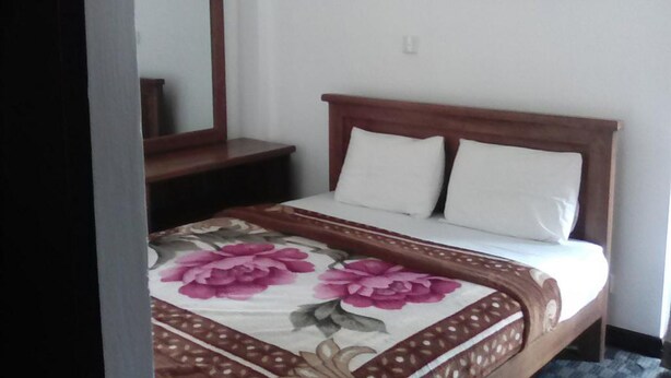 A bedroom with a wooden bed frame, white bedding, and a floral-patterned bedspread. - Ashley Hills (Nuwara Eliya)