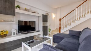 Una sala de estar moderna con un televisor de pantalla plana, una mesa de centro de vidrio, un sofá y una escalera con barandillas de madera.