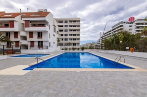 A swimming pool with a tiled deck, surrounded by modern buildings with balconies and a clear sky. - Altemar 2A004 totally refurbished (Playa de Las Americas)