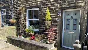 A stone house with a brick facade, a white window, and a green door. There are potted plants and a stone bench in front. - Character Cottage in Haworth. Come and Enjoy Yorkshire...Yours To Discover! (Haworth)