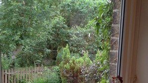 A window with a view of a garden, a wooden fence, and a chicken feeder. - Character Cottage in Haworth. Come and Enjoy Yorkshire...Yours To Discover! (Haworth)