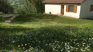 A house with a red-tiled roof, a white exterior, and wooden shutters. There is a grassy area with white and yellow flowers in front of the house. - Secluded house in the mountains with garden (Pergola)