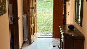 A hallway with a wooden door leading to a garden, a radiator, and a dark wooden cabinet with a bowl on top. - Secluded house in the mountains with garden (Pergola)
