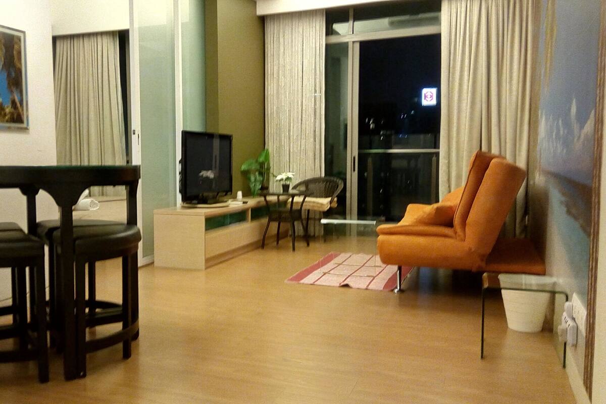 Un salon comprenant un téléviseur, un canapé, une table à manger avec des chaises et une fenêtre avec des rideaux.