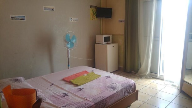 Un dormitorio con cama, ventilador, microondas y televisor en la pared.