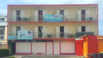 Un edificio de dos pisos con un letrero que dice 'Hotel Le Cap Vert' y un letrero de 'WORLD SHOP' debajo.