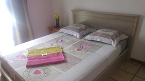 Una cama bien hecha con ropa de cama estampada, una mesita de noche con un florero y una ventana con cortinas.