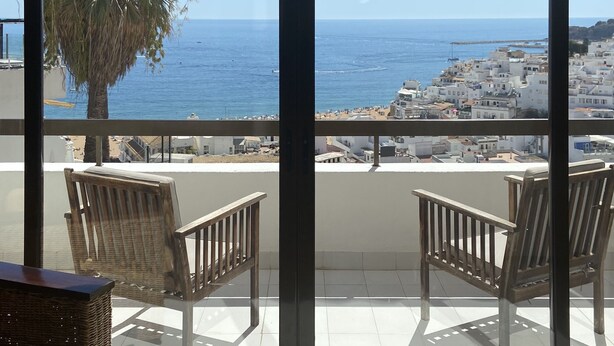Un balcone con sedie in vimini, vista sul mare e su una cittadina costiera.
