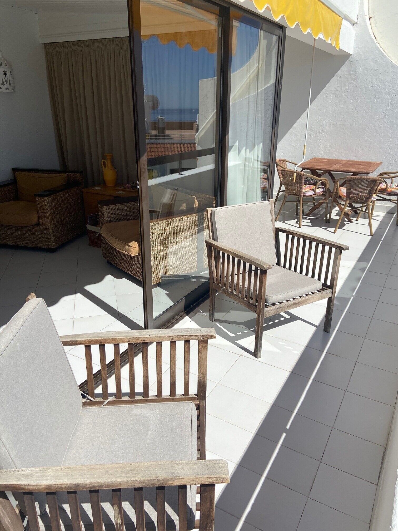 A sunlit balcony with wicker furniture, a glass door, and a yellow awning.