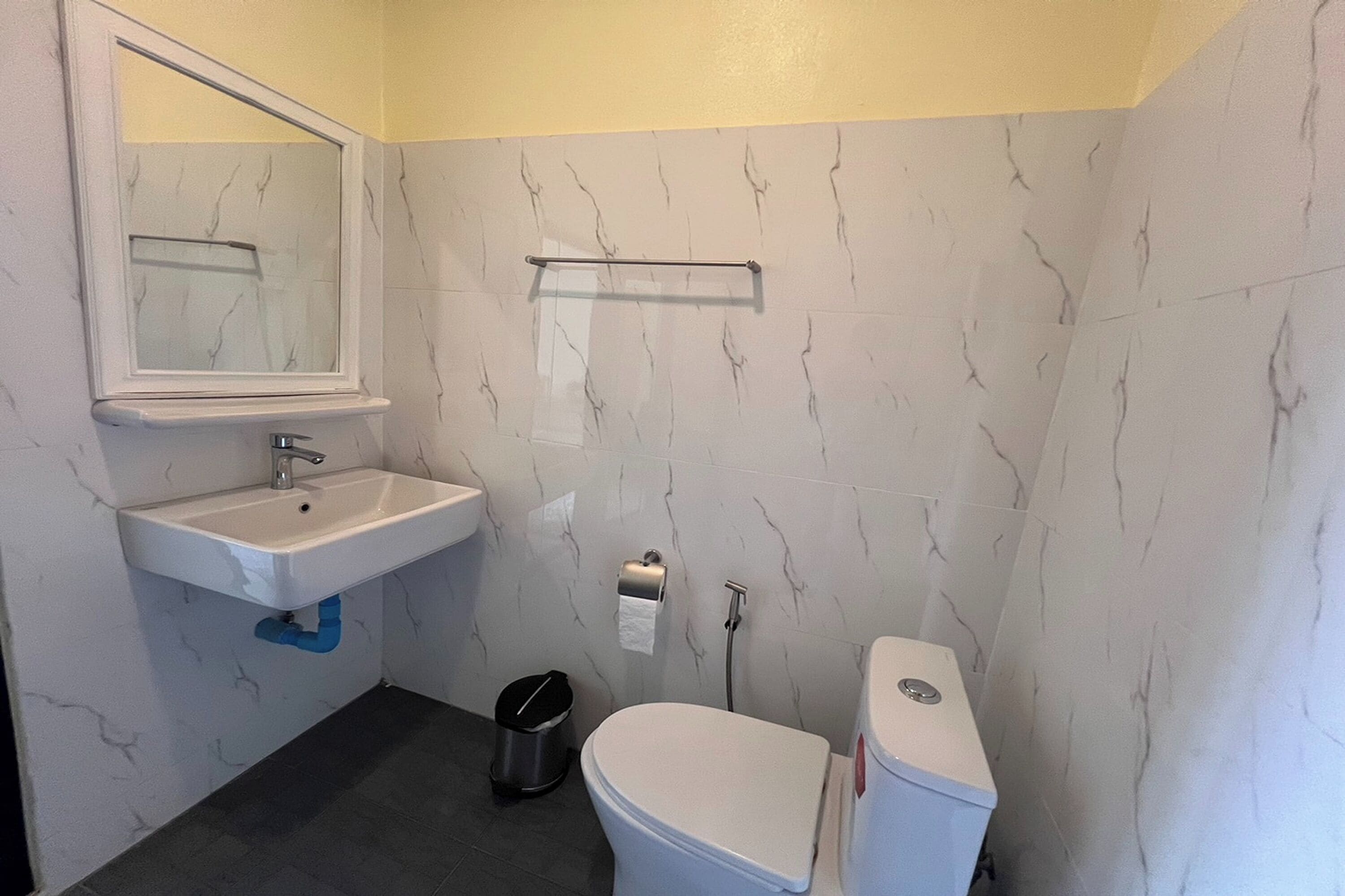 A bathroom with a white sink, mirror, toilet, and a trash bin.