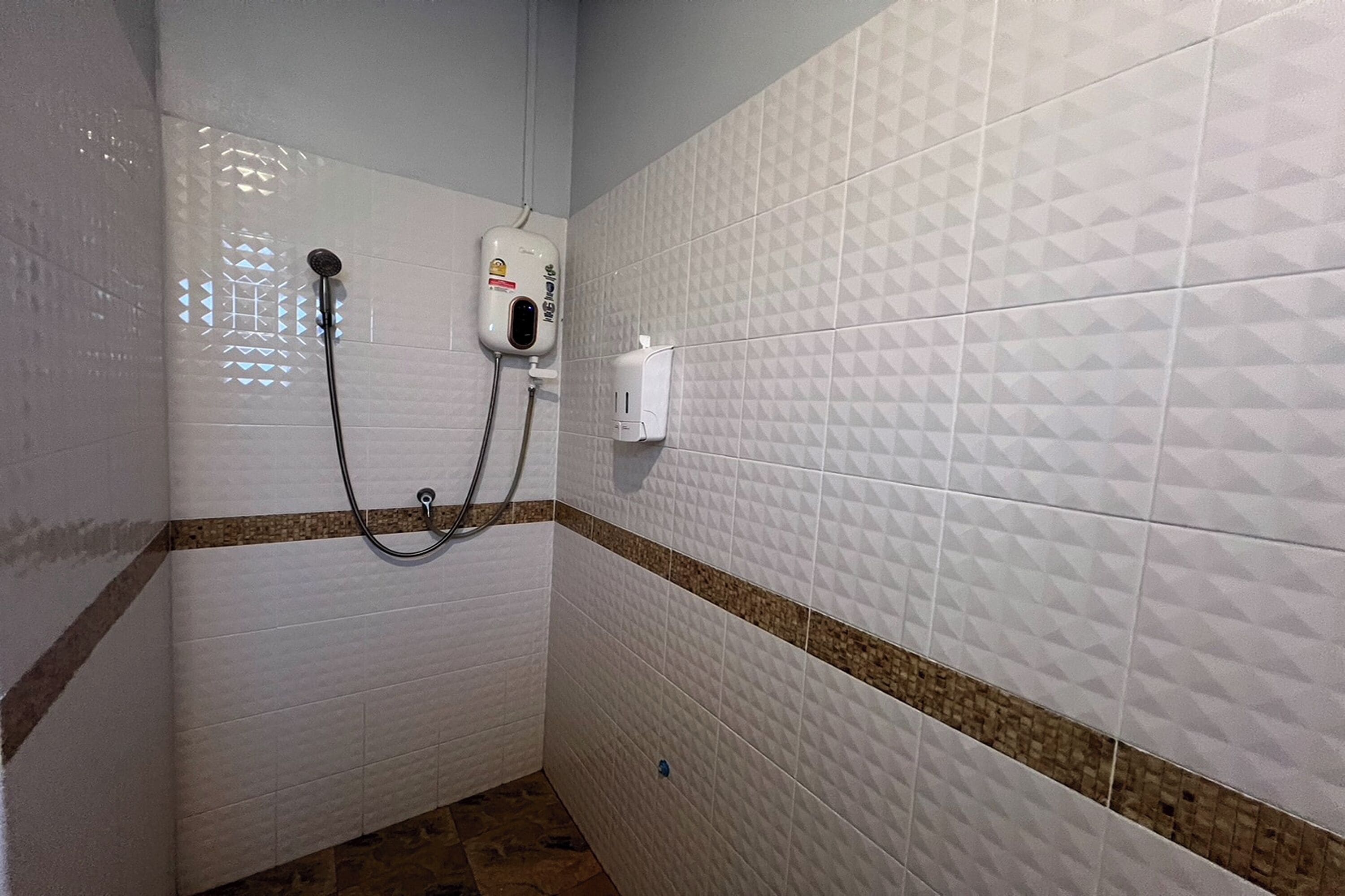 A bathroom with white tiled walls, a shower with a handheld showerhead, and a soap dispenser mounted on the wall.