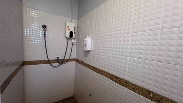 A bathroom with white tiled walls, a shower with a handheld showerhead, and a soap dispenser mounted on the wall.