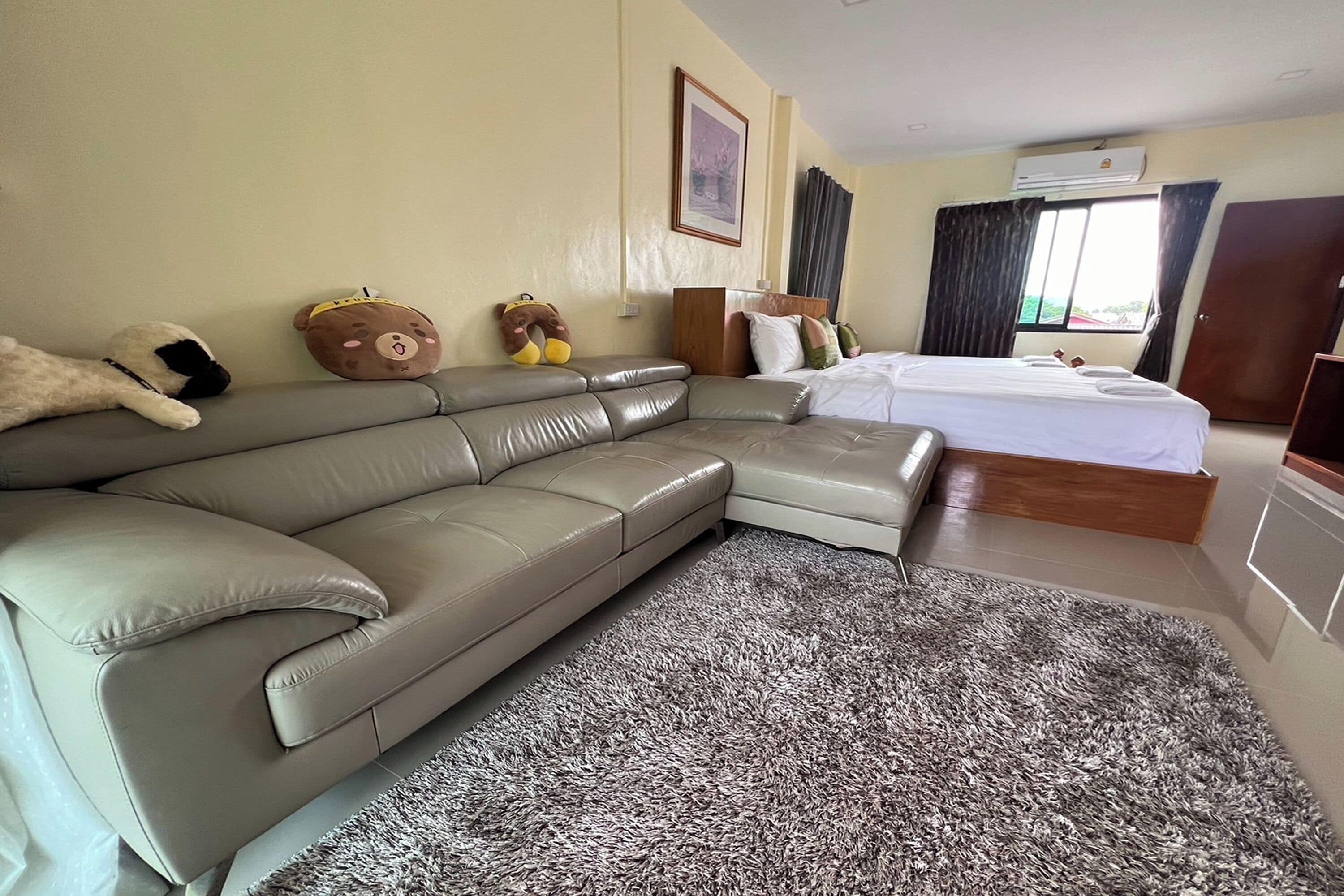 Ett modernt hotellrum med en grå lädersoffa, en stor, lurvig grå matta, en säng med vita sängkläder och en sänggavel i trä.