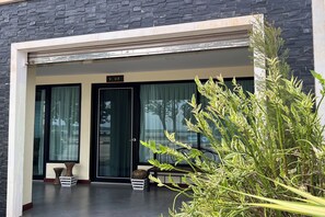 A modern building entrance with a black door, large windows, and a small outdoor seating area with a bench and two decorative tables.