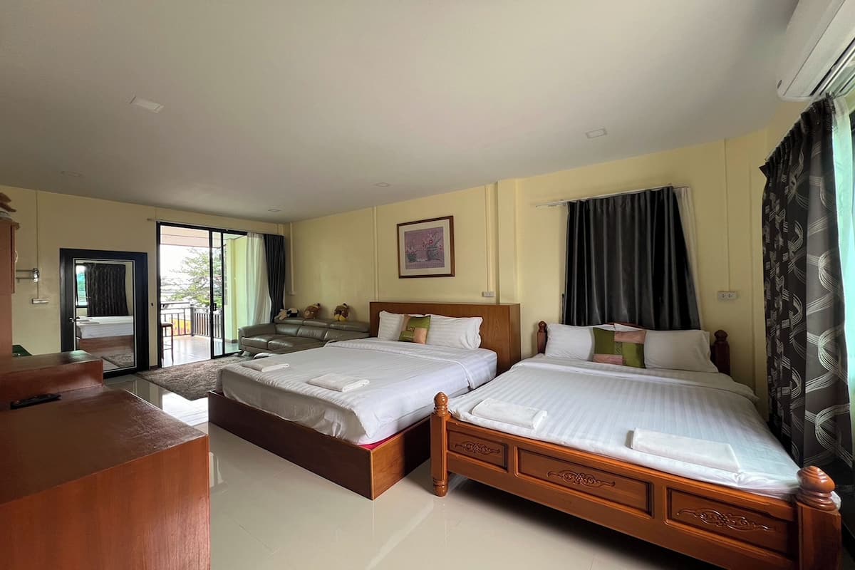 A hotel room with two wooden beds, a desk, a chair, a balcony, and a large window with curtains.