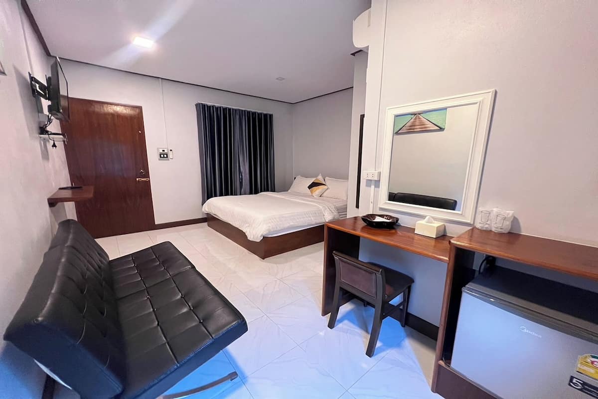 A hotel room with a bed, a desk, a chair, a TV, and a small refrigerator.