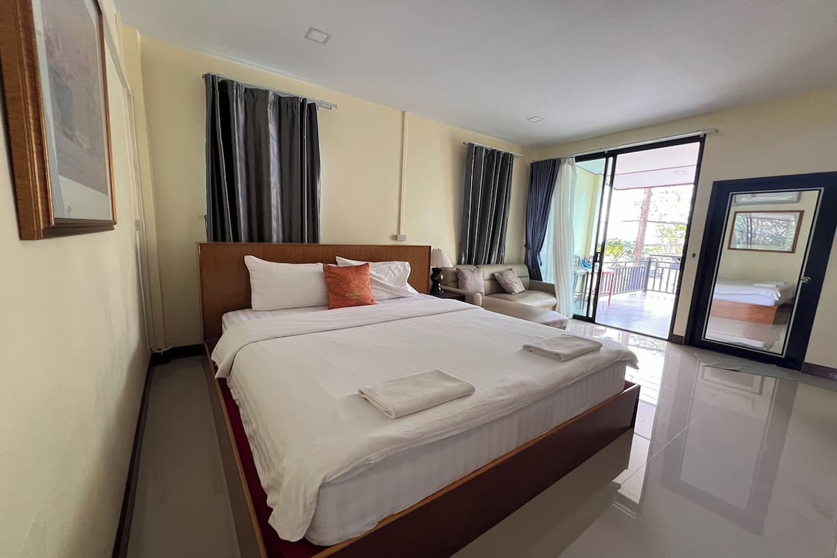 A hotel room with a large bed, a sofa, a sliding glass door to the balcony, and a framed picture on the wall.