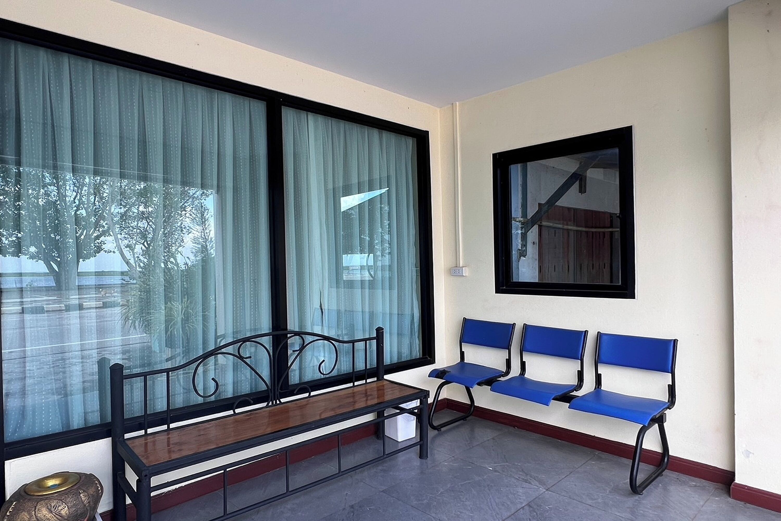 A waiting area with a bench and blue chairs, large windows with curtains, and a wall-mounted picture frame.