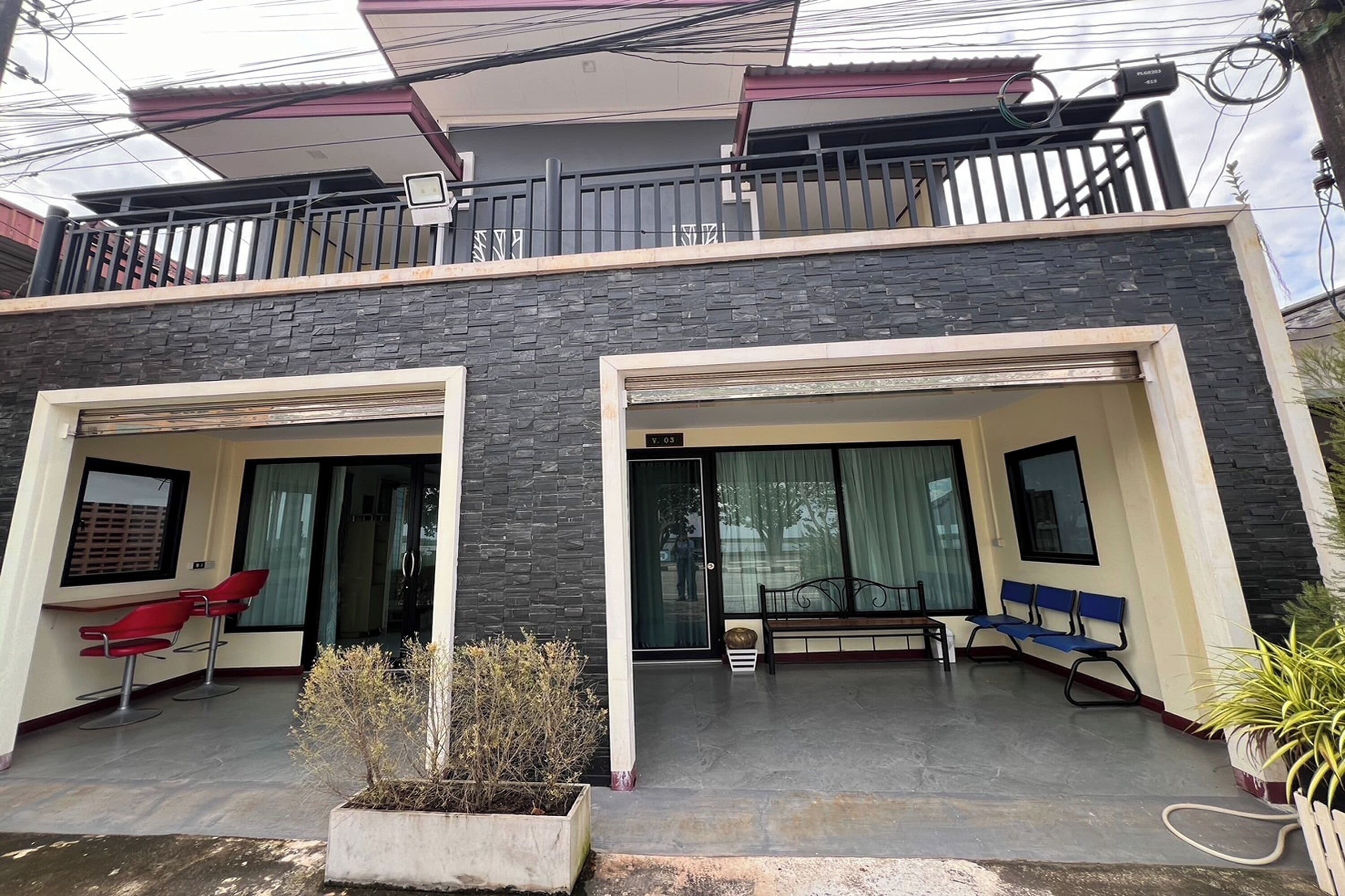 Un bâtiment moderne à deux étages, doté d’un balcon, de grandes fenêtres et d’un espace extérieur aménagé pour s’asseoir.