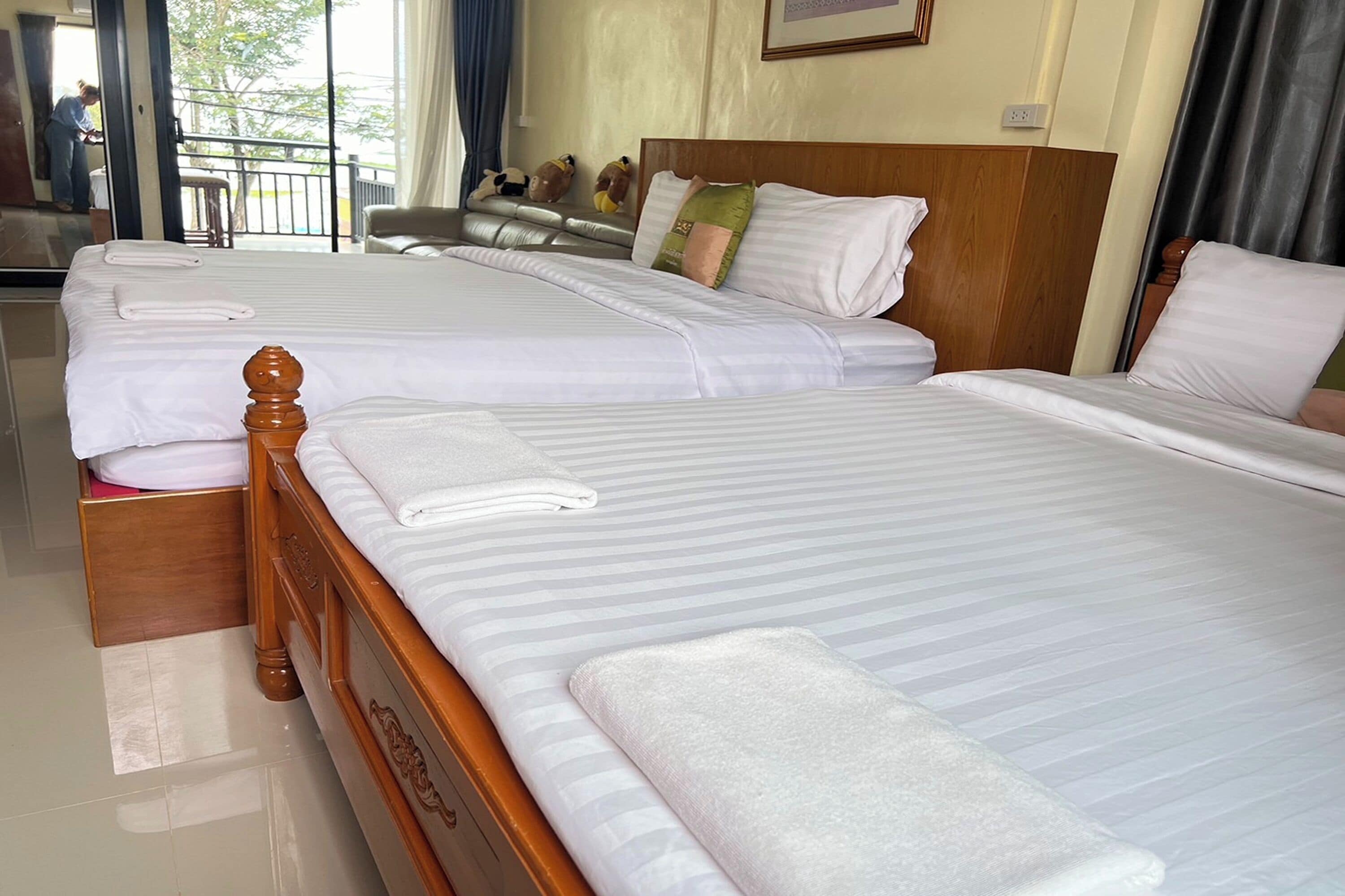Habitación de hotel con dos camas, cada una con sábanas blancas y cabeceros de madera. Hay toallas sobre las camas y se ve una ventana con cortinas.