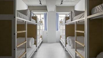 Quarto com beliches, um pilar branco no centro e uma janela com cortinas.