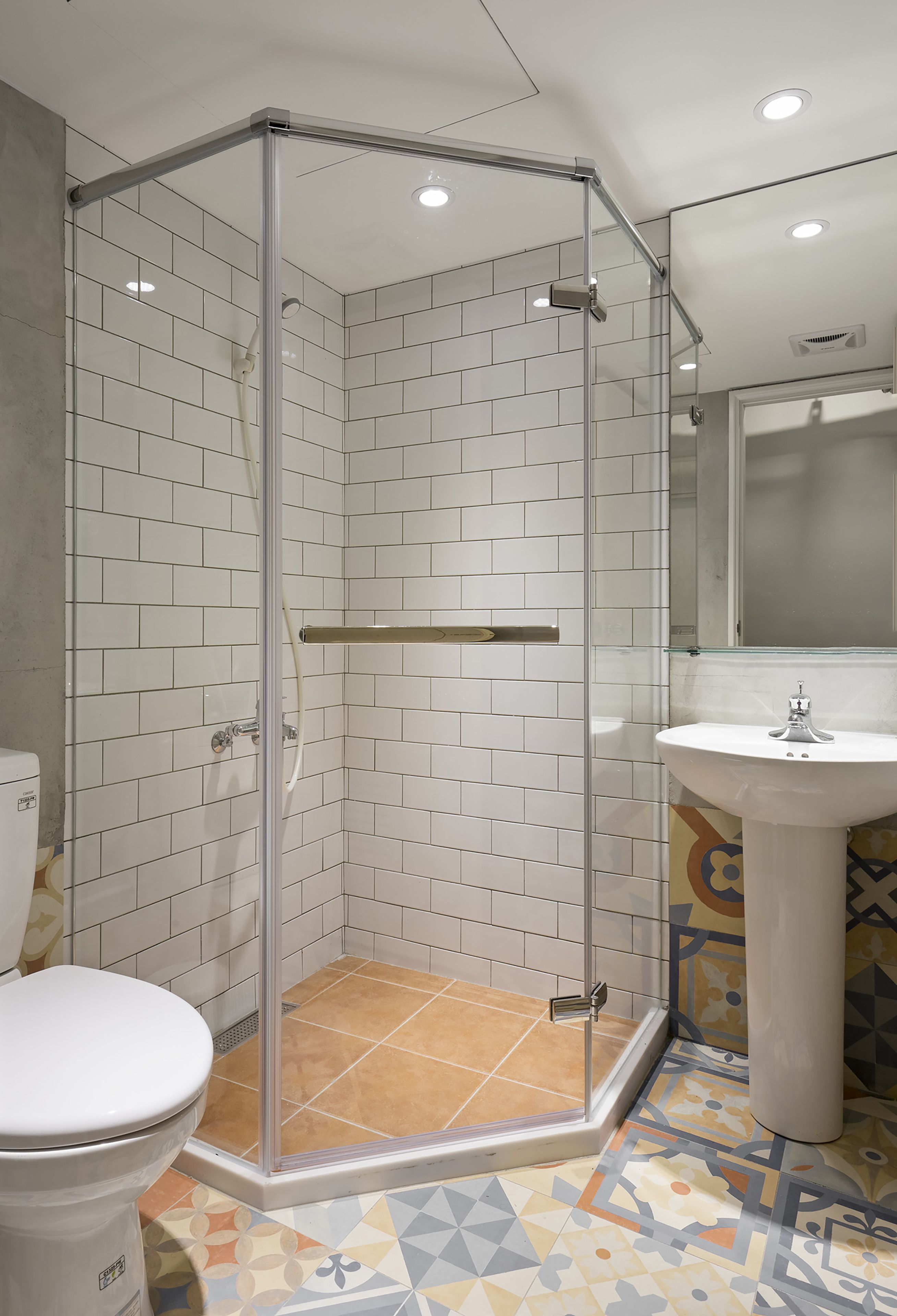 A bathroom with a glass-enclosed shower, white tiled walls, a white sink, and a patterned floor.