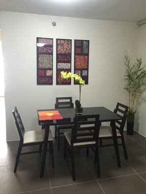 Zona pranzo con tavolo e quattro sedie, un vaso con fiori gialli e una parete con tre quadri incorniciati.