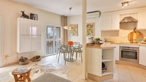 Una cocina moderna con horno empotrado, un comedor con mesa y sillas de vidrio, y una pequeña zona de estar con alfombra y taburetes.