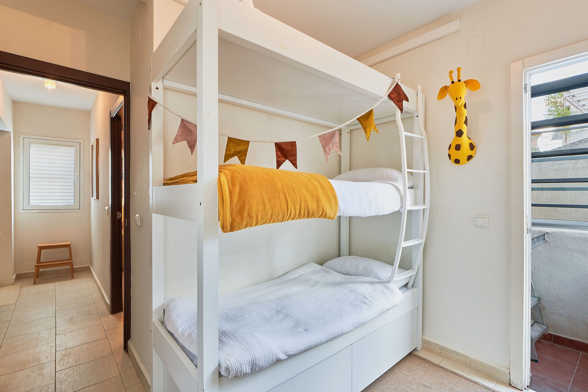 Une chambre avec un lit superposé, une échelle, une petite table et un motif décoratif représentant une girafe.