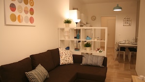 A living room with a brown sectional sofa, a white shelving unit with decorative items, and a dining area with a table and chairs. - Casa Palladio, in the heart of the historic center  (Vicenza)