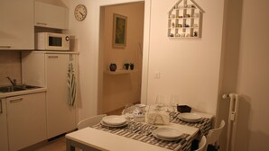 A compact kitchen with a microwave, sink, and cabinets. A dining table with plates and glasses is set for two. - Casa Palladio, in the heart of the historic center  (Vicenza)