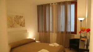 A hotel room with a bed, a desk, a chair, a lamp, and a window with curtains. - Casa Palladio, in the heart of the historic center  (Vicenza)