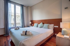 Ein Hotelzimmer mit einem großen Bett, einem Holzkopfstück, einem Nachttisch mit Lampe und Blick auf einen Balkon durch das Fenster.
