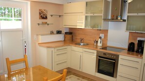 Een kleine keuken met houten kastjes, een spoelbak, een fornuis en een eettafel met stoelen.