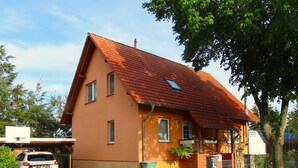 Een huis met twee verdiepingen, voorzien van een rode dakbedekking, een fundering van baksteen en een geplaveid oprit.