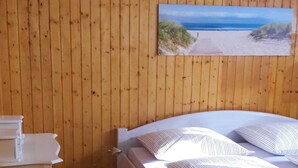Een kamer met houten lambrisering, een bed, een bureau en een schilderij van een strand.