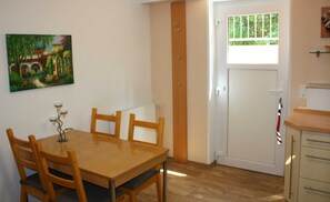 Un comedor con mesa y sillas de madera, un radiador, una puerta con ventanal y un cuadro en la pared.