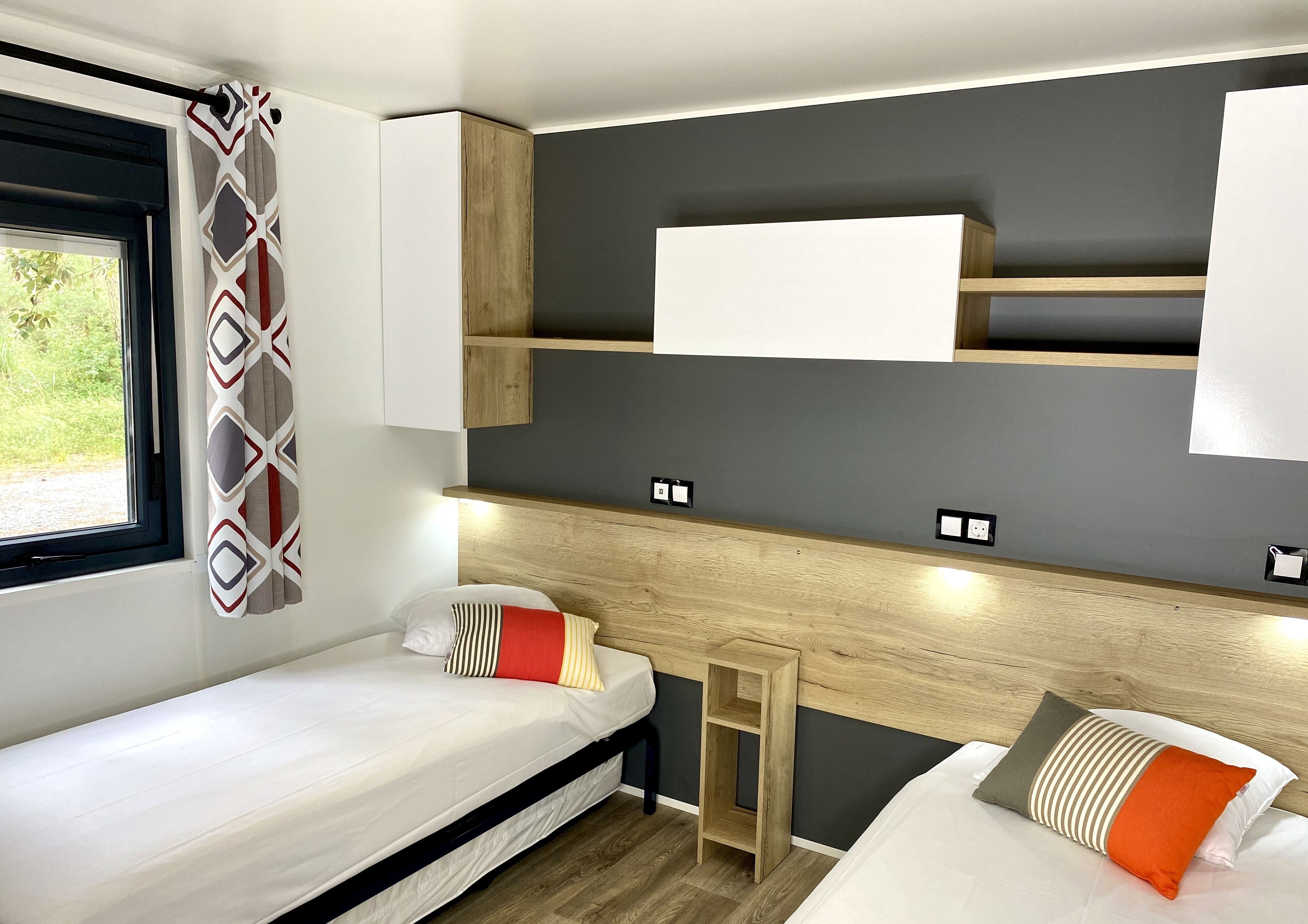 A compact room with two beds, a window, and built-in shelves.