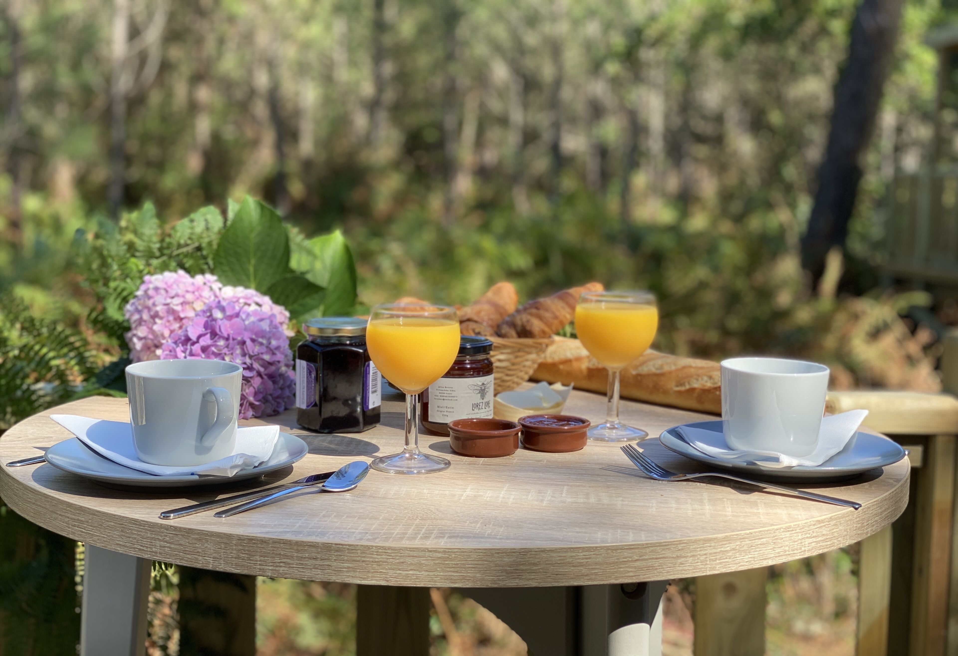 A breakfast table with cups, glasses, bread, and condiments.
