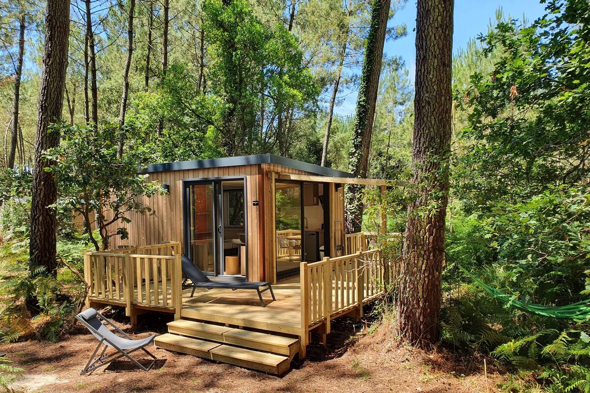 A wooden cabin with a deck, a lounge chair, and a glass door leading inside.