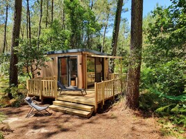 A wooden cabin with a deck, a lounge chair, and a glass door leading inside.